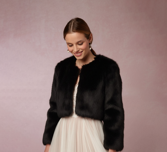 Mujer elegante con abrigo de peluche sintética negro, mirando a la cámara con pose natural y suave expresión. Abrigo de novia, estola negra, moda invierno, vestidos de fiesta, accesorios de boda.